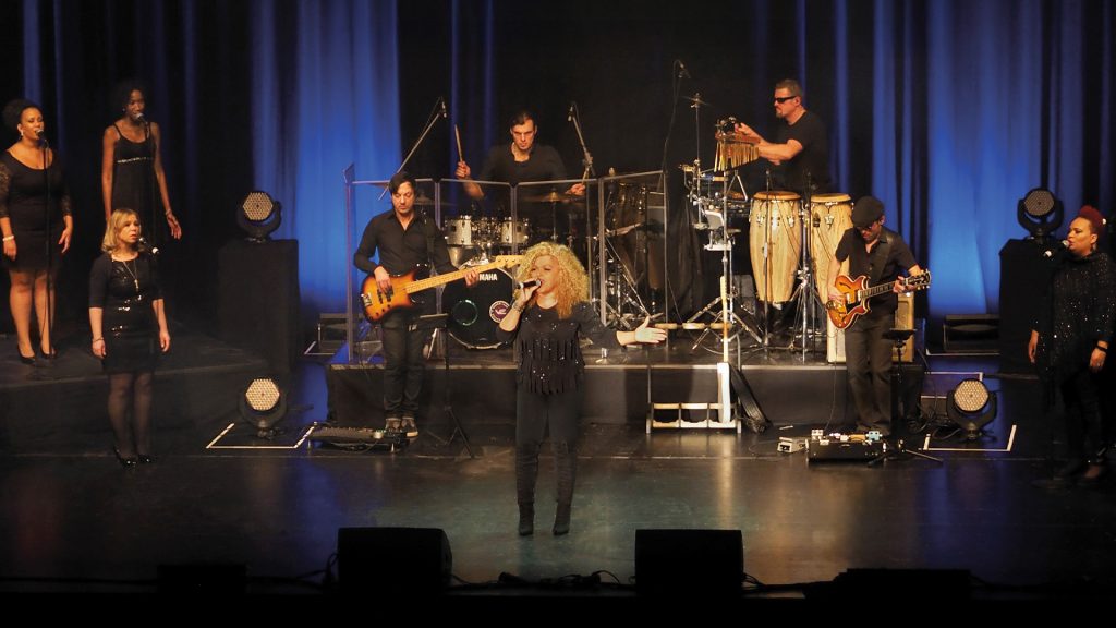 Eine Frau singt auf der Bühne, eine Band spielt im Hintergrund