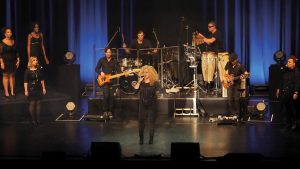 Eine Frau singt auf der Bühne, eine Band spielt im Hintergrund