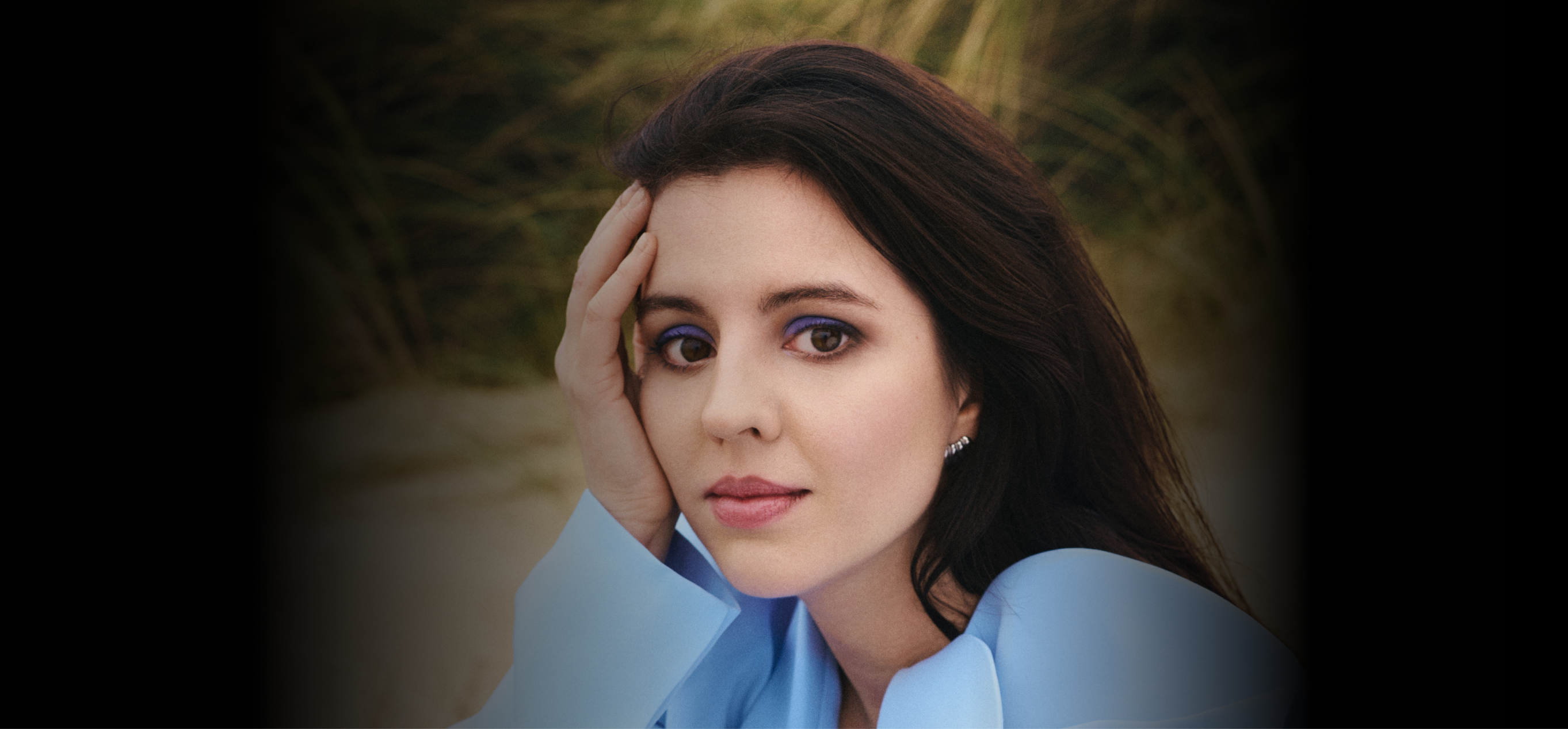 Eine Frau mit blauem Hemd und langen Haaren, welche in die Kamera schaut